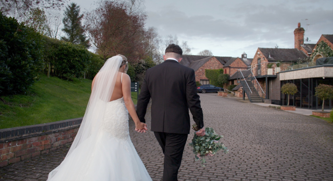 Image shows newlyweds Megan and Eden walking hand in hand around their wedding venue Moddershall Oaks in Staffordshire