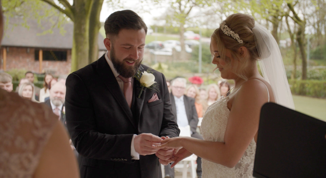 Image shows young couple Megan and Eden exchanging rings at their outdoor wedding at Moddershall Oaks in Staffordshire